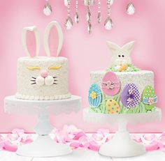 two cakes decorated with bunny ears and eggs on top of a cake stand next to pink flowers