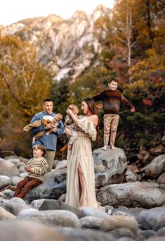 a family standing on rocks in the middle of a river with mountains in the background