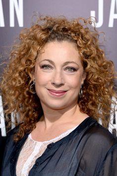 a woman with curly red hair smiling at the camera