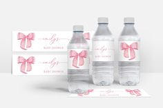 three water bottles with pink bows on them next to two baby shower cards and a place card