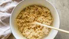 a white bowl filled with macaroni and cheese on top of a table next to a wooden spoon