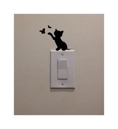 a black cat sitting on top of a white light switch cover with butterflies flying around it