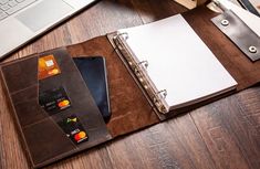 an open notebook sitting on top of a wooden desk next to a laptop and keyboard