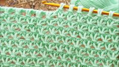 a green crochet with a yellow knitting needle next to it and another piece of yarn in the background