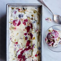 a pan filled with ice cream next to a spoon and bowl of fruit toppings