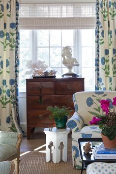 a living room filled with furniture and flowers on the window sill in front of a dresser