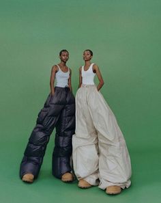 two women standing next to each other in front of a green background wearing white tops and black pants