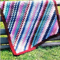 a colorful crocheted blanket sitting on top of a wooden bench in the grass