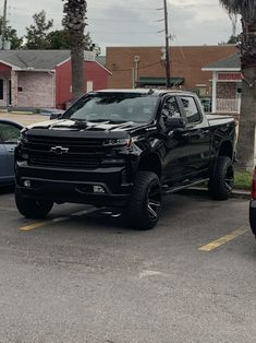 a black truck parked in a parking lot next to other cars and palm trees on a cloudy day