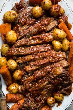 steak, potatoes and carrots on a white plate with a fork next to it