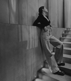 black and white photograph of woman leaning against wall with hand on hips, looking up