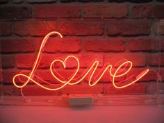 a neon sign with the word love written on it in front of a brick wall