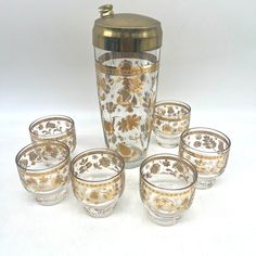 a set of six glass cups and a gold lidded vase with flowers on it