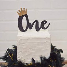 a white cake with black feathers and a gold crown on top that says, one