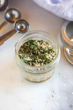 a glass jar filled with herbs next to measuring spoons