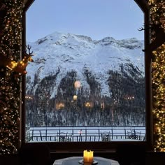 a candle is sitting on a table in front of a window with lights and snow covered mountains behind it