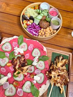 two pizzas with veggies and meat on them sitting on a wooden table