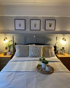 a bed with white sheets, pillows and two plants on the nightstands next to it