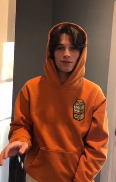 a young man in an orange hoodie is holding his hands out to the side