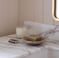 a white marble counter top with a soap dish on it next to a candle and mirror