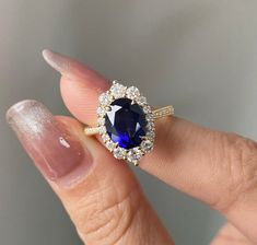 a woman's hand holding an oval shaped blue sapphire and diamond halo engagement ring