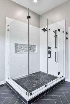 a walk in shower sitting next to a white tiled wall and black tile flooring