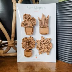 three wooden magnets with plants in them sitting on a table next to a chair