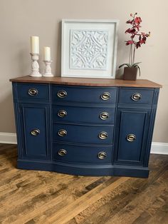 a blue dresser with two white candles on top and a framed photograph above it, in a living room