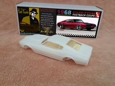 a white plastic model car in front of a box on a pink carpeted surface