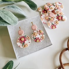 two pairs of earrings sitting on top of a white table next to some green plants