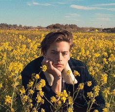 a young man sitting in a field of yellow flowers with his hands on his face