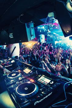 a dj mixing in front of a large crowd at a music event with his hands up