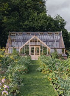 a greenhouse with lots of plants and flowers in the foreground, surrounded by trees