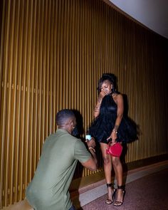 a man kneeling down next to a woman in a short black dress and high heels