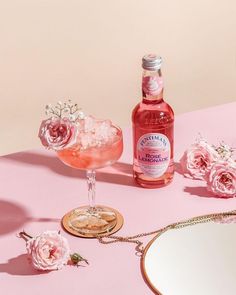 a pink table topped with a glass filled with liquid and flowers next to a mirror