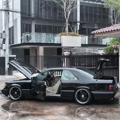 a black car parked in front of a building with its door open and it's hood up