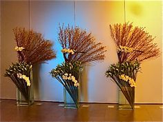 three vases filled with flowers sitting on top of a wooden table next to a wall