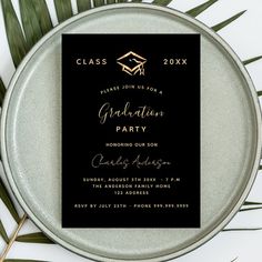 a black and gold graduation party card on top of a metal plate with palm leaves