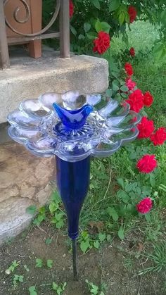 a blue glass birdbath sitting on top of a flower bed next to red flowers