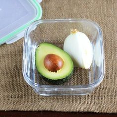 an avocado cut in half sitting on top of a table next to a plastic container