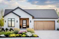 a white house with two garages and flowers in the front yard on a sunny day