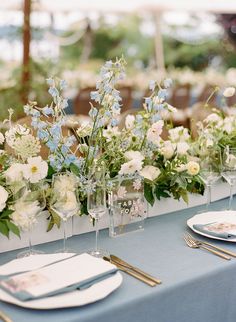 the table is set with blue and white flowers in vases, silverware, and napkins