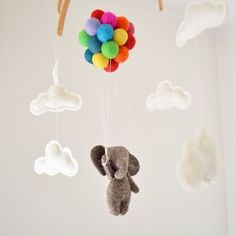 a stuffed elephant hanging from a mobile with clouds and rainbow balls on it's back