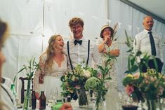 a group of people standing next to each other at a table with flowers in vases