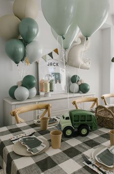 a table topped with balloons and plates next to a green truck on top of a checkered table cloth