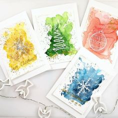 four cards with watercolor designs on them, one has a christmas ornament