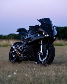 a black motorcycle parked on top of a dry grass field next to a forest at dusk