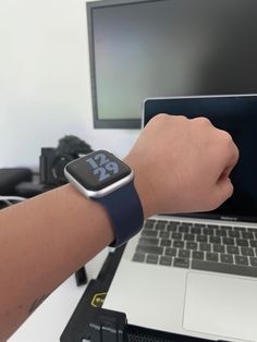 an apple watch is being held by someone's hand near a laptop and monitor