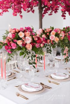 the table is set with pink and red flowers in vases, candles, and plates