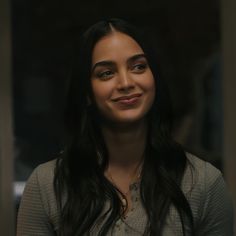 a woman with long black hair smiles at the camera while standing in front of a mirror